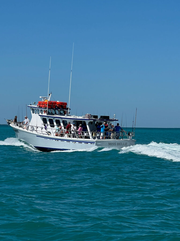 A boat carrying about 30 people in the water. "Miss Belle" written on the stern. 